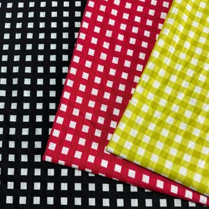 May include: Three pieces of fabric featuring a classic gingham check pattern. The first piece is black and white, the second is red and white, and the third is lime green and white. Each fabric displays a consistent grid of small squares.