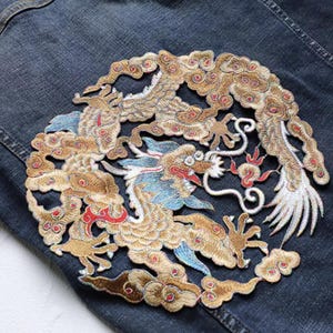 May include: Embroidered patch with a golden dragon design, featuring red, blue, and white details, set against a dark denim background. The dragon is intricately stitched in a circular pattern.