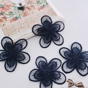 Puede incluir: Cuatro apliques florales azul marino con un diseño delicado y en capas. Cada flor tiene una capa exterior transparente de color claro y un centro más oscuro y texturizado. Estos adornos son ideales para manualidades.