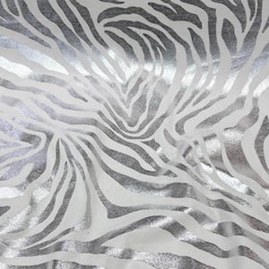 Puede incluir: Primer plano de una tela con un estampado de rayas de cebra. El diseño presenta rayas plateadas sobre un fondo blanco. La tela tiene un ligero brillo, lo que le da un aspecto lujoso. El patrón es consistente en todo el material, creando un diseño audaz y llamativo.