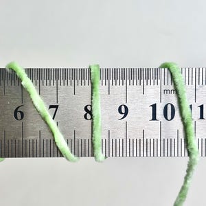 Puede incluir: Primer plano de hilo verde claro junto a una regla met&aacute;lica. El hilo es esponjoso y parece estar hecho de un material suave. La regla muestra medidas en mil&iacute;metros, con el hilo que abarca de 6 a 11 mm.