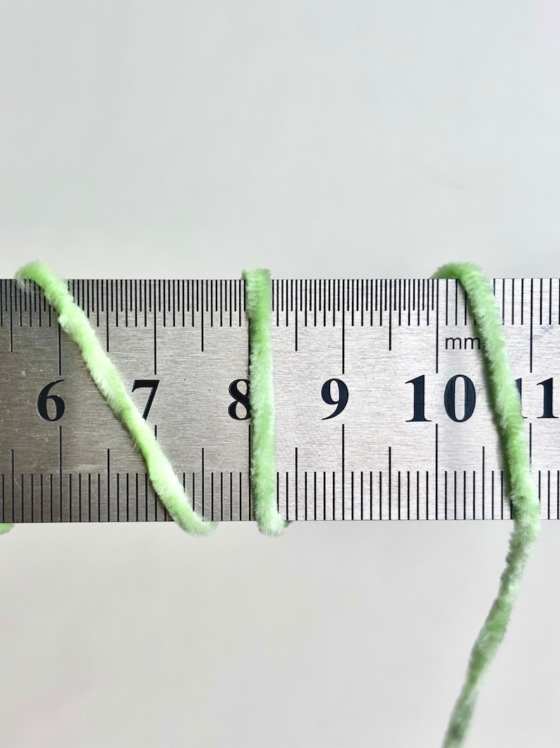 Puede incluir: Primer plano de hilo verde claro junto a una regla met&aacute;lica. El hilo es esponjoso y parece estar hecho de un material suave. La regla muestra medidas en mil&iacute;metros, con el hilo que abarca de 6 a 11 mm.