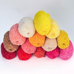 Puede incluir: Una colecci&oacute;n de ovillos de lana coloridos en tonos amarillos, rosas, rojos, naranjas, marrones y crema. Los ovillos de lana est&aacute;n apilados, creando una exhibici&oacute;n visualmente atractiva. Ideal para proyectos de tejido y ganchillo.