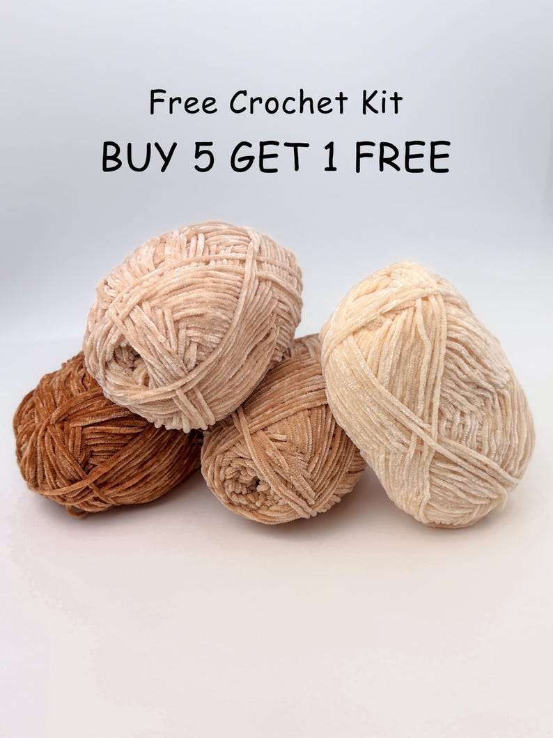 Puede incluir: Un conjunto de cinco ovillos de lana en tonos marrones y beige. La lana tiene una textura suave y aterciopelada. El texto "Free Crochet Kit" y "BUY 5 GET 1 FREE" se muestra encima de la lana.