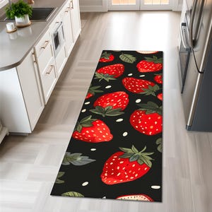 May include: A rectangular kitchen runner rug featuring a repeating pattern of large, ripe red strawberries with green leaves and white dots on a black background. The rug is placed on a light wood floor.