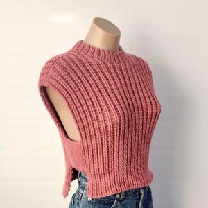 May include: A dusty rose-colored, sleeveless knitted top with a ribbed texture. The top has a high, rounded neckline and a split design on the sides. The garment is displayed on a mannequin.