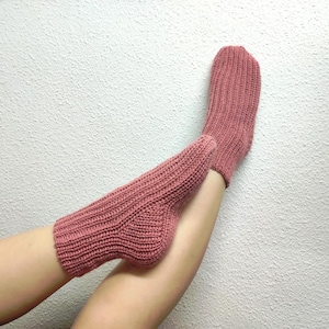 Pode incluir: Um par de meias de malha na cor rosa empoeirado. As meias são caneladas e parecem feitas à mão. São exibidas sobre um fundo branco texturizado.