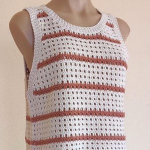 May include: A cream-colored crochet top with horizontal rust-colored stripes. The sleeveless top has a scoop neckline and a loose, open weave design. The top is displayed on a mannequin.