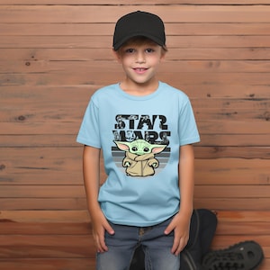 以下が含まれることがあります： スターウォーズのグローグのグラフィックが特徴のライトブルーのTシャツ。 「STAR WARS」の文字がグローグのグラフィックの上に黒で印刷されています。 子供は黒い野球帽とブルージーンズを着用しています。