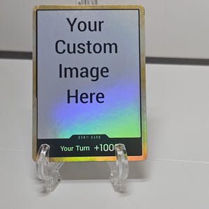 May include: A custom image card with the text "Your Custom Image Here" in a bold, black font. The card has a holographic border and is displayed on a clear plastic stand. The text "Your Turn +100" is also visible.