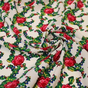 Peut inclure: Tissu blanc orné d'un motif floral. De grandes roses rouges sont associées à des feuilles vertes, des baies bleues et des touches de jaune. Le tissu est plié, révélant la texture et le motif.