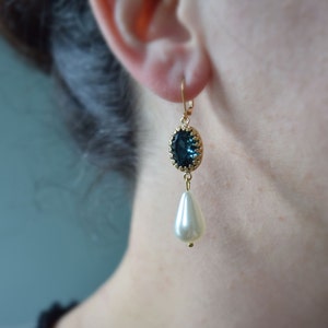 May include: Gold dangle earrings featuring a dark blue oval-shaped gemstone and a white pearl drop.