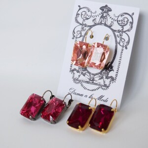 May include: Three pairs of dangle earrings with gold and silver hooks. The earrings feature pink, light pink, and red rectangular gemstones.