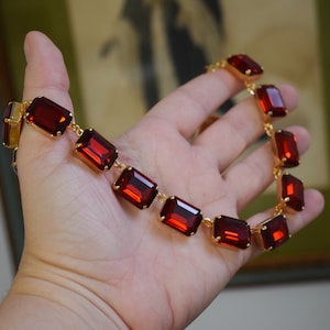 May include: A gold necklace with a chain and large, rectangular, red gemstones.
