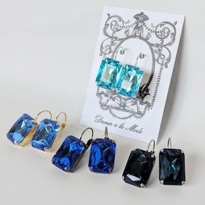May include: Three pairs of earrings with large rectangular gemstones. The first pair is turquoise blue, the second pair is a darker blue, and the third pair is a dark teal.