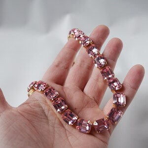 May include: A pink crystal necklace with gold accents. The necklace is made of rectangular-shaped crystals.