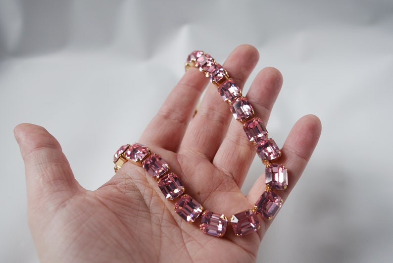 May include: A pink crystal necklace with gold accents. The necklace is made of rectangular-shaped crystals.