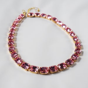 May include: A pink crystal necklace with gold accents. The necklace is made of rectangular-shaped crystals.