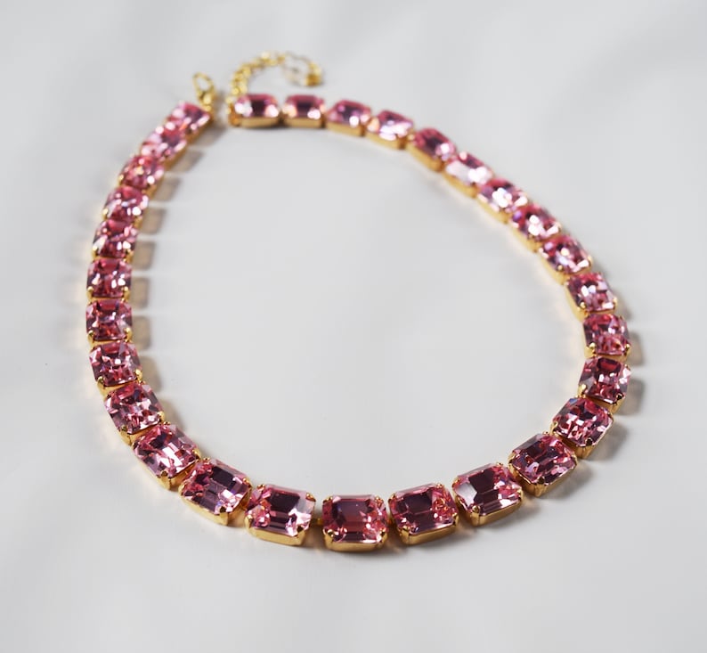 May include: A pink crystal necklace with gold accents. The necklace is made of rectangular-shaped crystals.