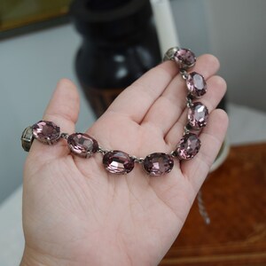 May include: A silver necklace with a row of oval-shaped, light purple rhinestones.