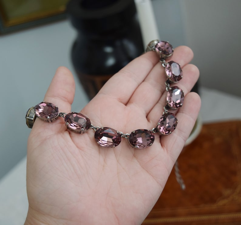 May include: A silver necklace with a row of oval-shaped, light purple rhinestones.