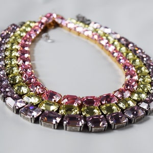 May include: A multi-layered necklace with large, rectangular, faceted crystals in shades of pink, yellow, and lavender.