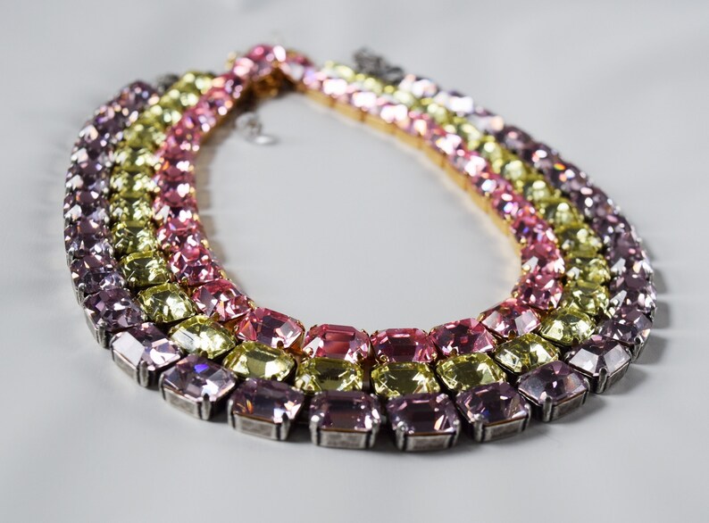 May include: A multi-layered necklace with large, rectangular, faceted crystals in shades of pink, yellow, and lavender.