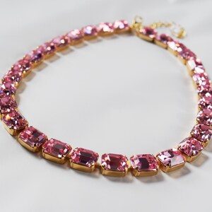 May include: A pink crystal choker necklace with gold-toned metal accents. The necklace is made of rectangular-shaped crystals.