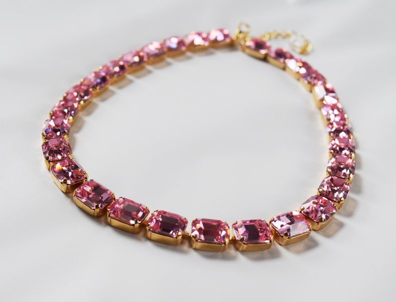 May include: A pink crystal choker necklace with gold-toned metal accents. The necklace is made of rectangular-shaped crystals.