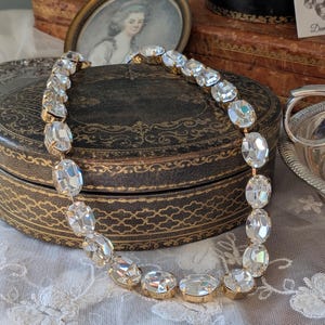 Puede incluir: Un collar que presenta una serie de cristales transparentes de forma ovalada y tallados, engarzados en metal de tono dorado. Los cristales est&aacute;n unidos en una fila continua, creando un dise&ntilde;o de cadena flexible que refleja la luz.