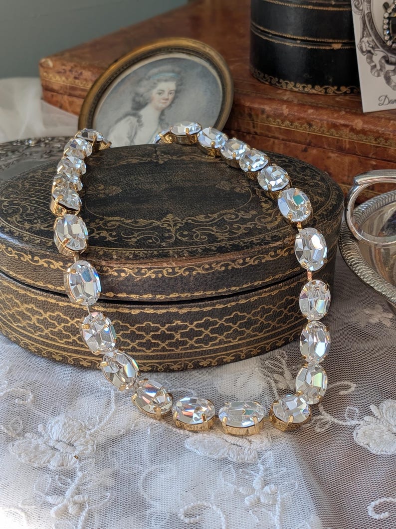 Puede incluir: Un collar que presenta una serie de cristales transparentes de forma ovalada y tallados, engarzados en metal de tono dorado. Los cristales est&aacute;n unidos en una fila continua, creando un dise&ntilde;o de cadena flexible que refleja la luz.
