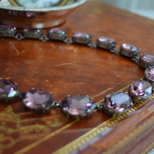 May include: A purple crystal necklace with oval-shaped stones set in silver-toned metal.