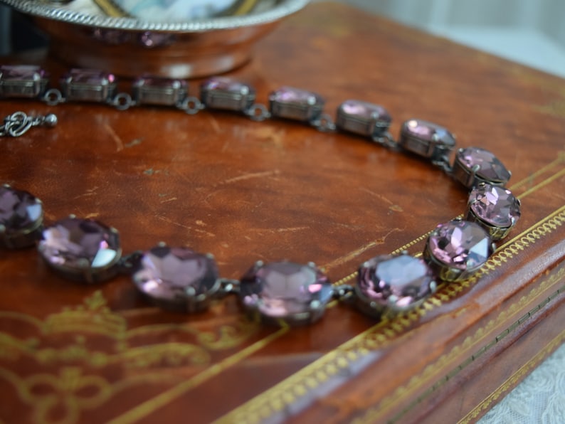 May include: A purple crystal necklace with oval-shaped stones set in silver-toned metal.