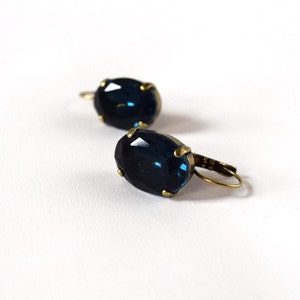Puede incluir: Un par de pendientes de estilo vintage con grandes piedras preciosas ovaladas de color azul oscuro. Las piedras est&aacute;n engastadas en un metal color lat&oacute;n con cierre de palanca. Fondo blanco.