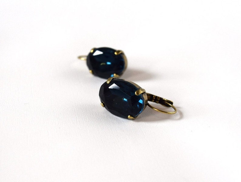 Puede incluir: Un par de pendientes de estilo vintage con grandes piedras preciosas ovaladas de color azul oscuro. Las piedras est&aacute;n engastadas en un metal color lat&oacute;n con cierre de palanca. Fondo blanco.