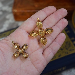 May include: Two gold-tone cross charms with amber-colored crystal accents. The larger charm has five crystals and the smaller charm has four crystals.