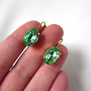 May include: A pair of gold earrings with oval-shaped green gemstones.