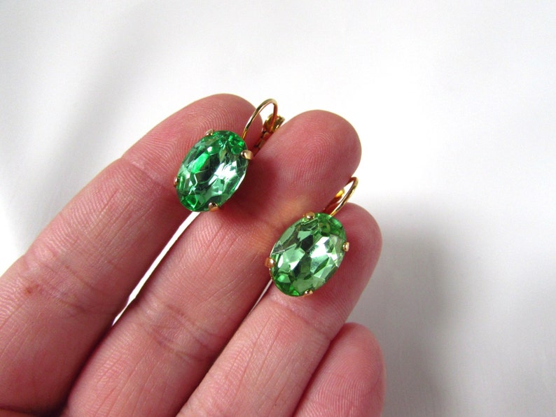 May include: A pair of gold earrings with oval-shaped green gemstones.