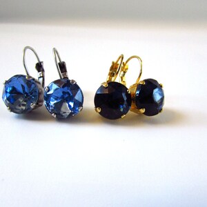 May include: A pair of earrings with blue and black crystal stones. The earrings have silver and gold-toned hooks.