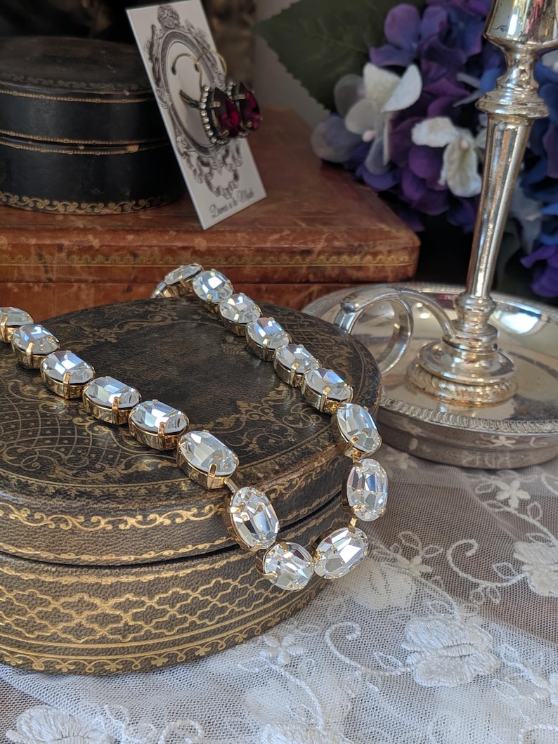 Puede incluir: Un collar que presenta una serie de cristales transparentes de forma ovalada y tallados, engarzados en eslabones de metal dorado. Los cristales est&aacute;n dispuestos en una fila continua, reflejando la luz con gran brillo.