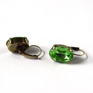 May include: A pair of green gemstone earrings with gold-toned metal settings. The earrings have a simple, oval-shaped design.