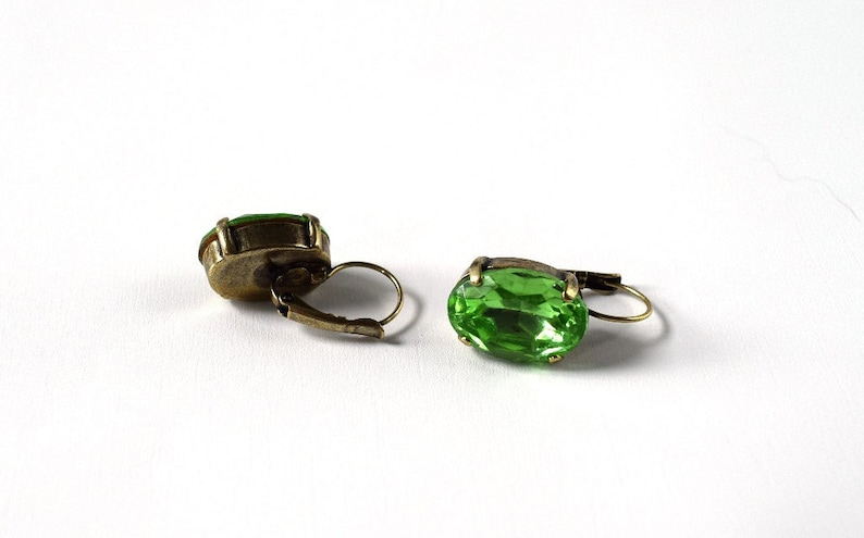 May include: A pair of green gemstone earrings with gold-toned metal settings. The earrings have a simple, oval-shaped design.