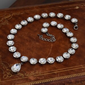 May include: A silver necklace with a teardrop pendant made of clear crystals. The necklace is made of a chain of round, clear crystals.