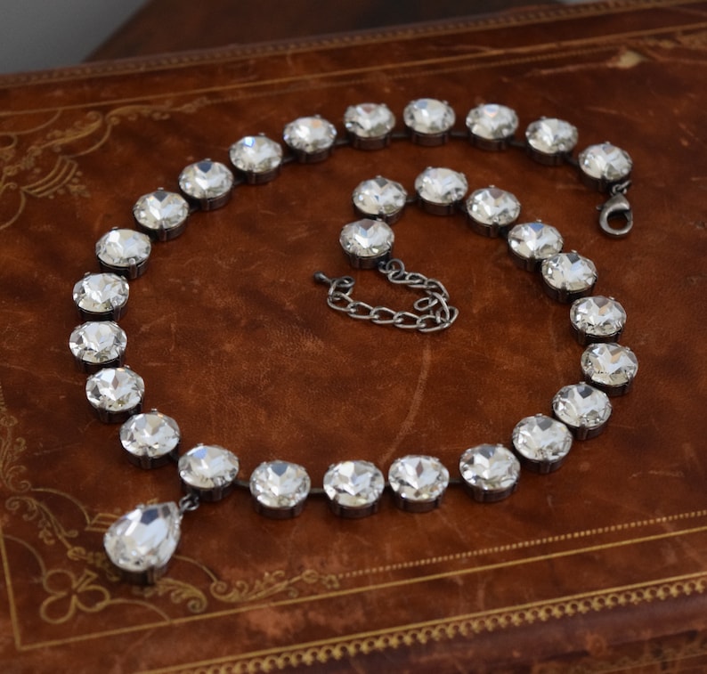 May include: A silver necklace with a teardrop pendant made of clear crystals. The necklace is made of a chain of round, clear crystals.