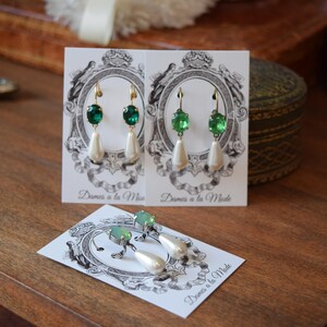 May include: Elegant green and white drop earrings with a pearlescent teardrop shape. The earrings have a gold-colored hook and are displayed on a card with the text "Dames a la Mode".