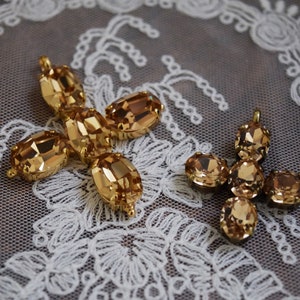 May include: Two gold-toned metal charms with amber-colored crystal embellishments. The charms are shaped like a cross and a flower.