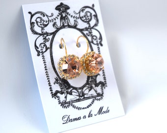Puede incluir: Un par de pendientes de oro con piedras de cristal de color melocotón. Los pendientes están en una tarjeta blanca con el texto "Dames a la Mode".