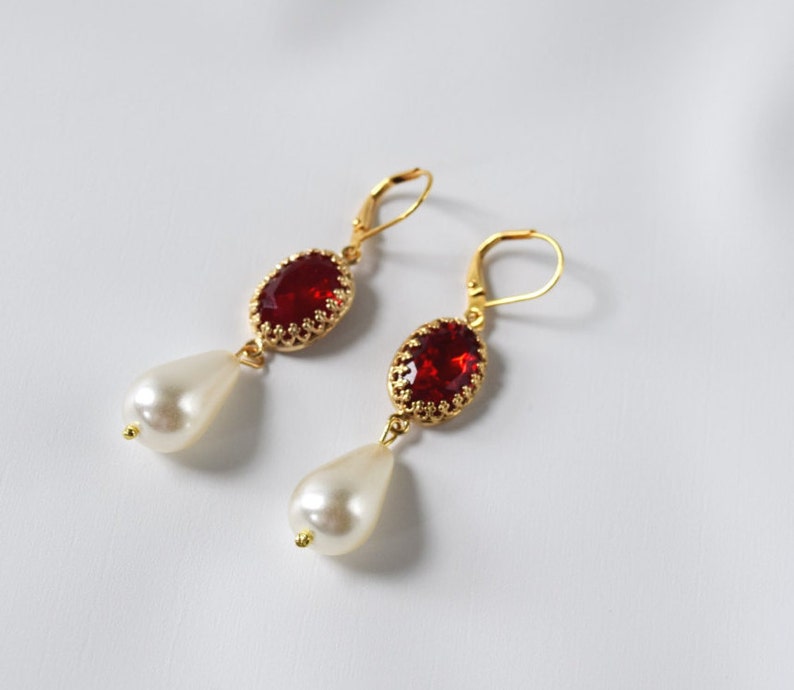 May include: A pair of gold earrings with red gemstone and white pearl drops.