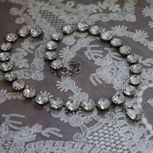 May include: A silver necklace with clear crystal beads on a white lace background.