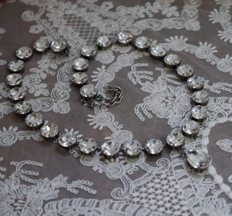 May include: A silver necklace with clear crystal beads on a white lace background.